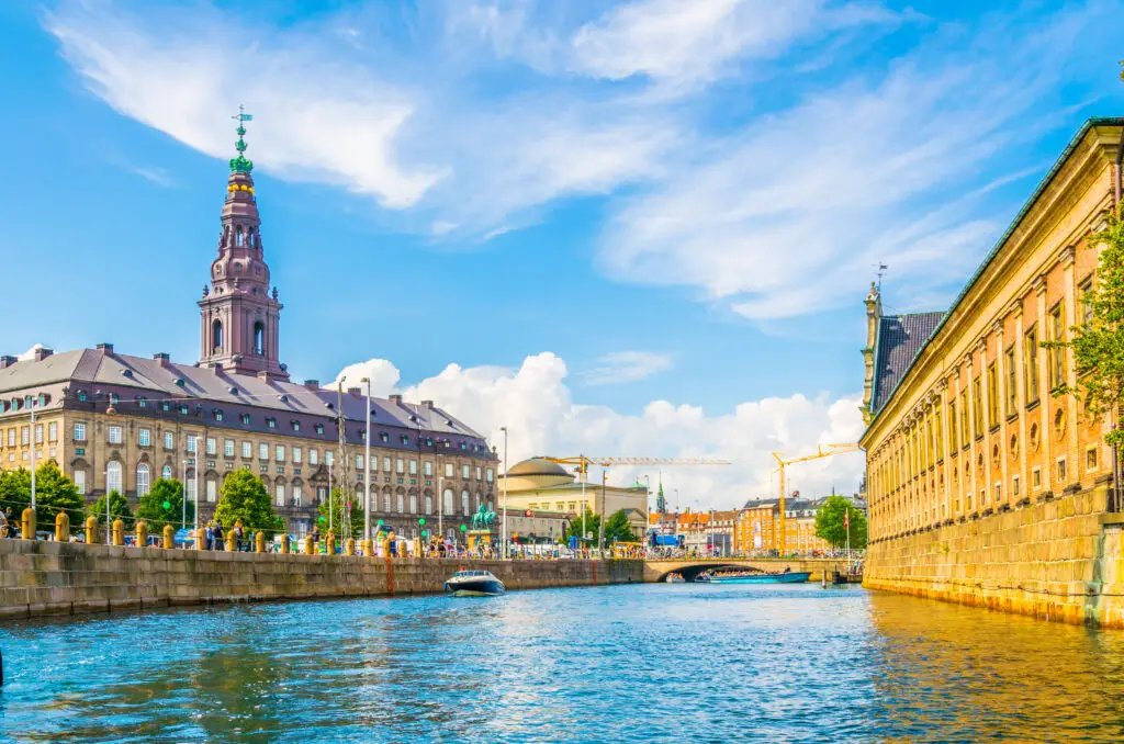 View of Christiansborg Slot Palace along the canal in Copenhagen, Denmark, showcasing the historic architecture and vibrant urban life.