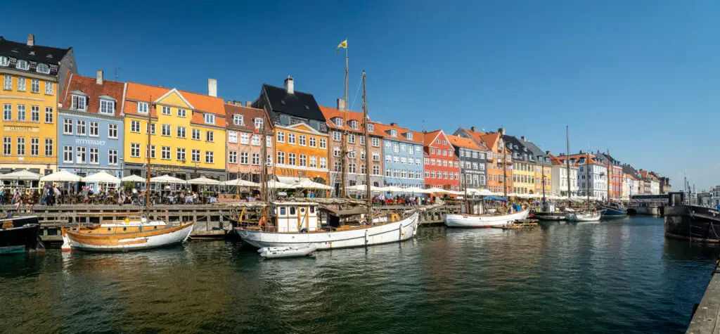 Panoramic view of colorful 17th-century buildings along Nyhavn canal with historical wooden ships in Copenhagen, Denmark, a popular tourist destination in Scandinavia.