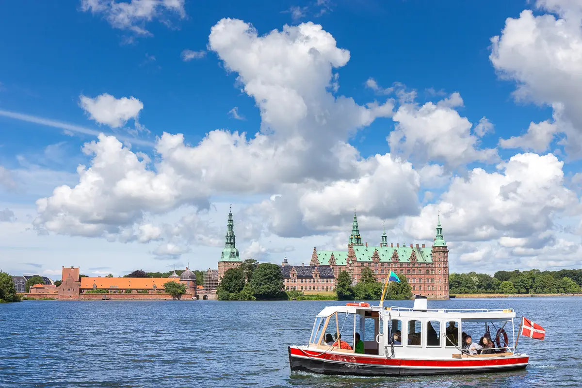 Tourists enjoy a boat tour on a picturesque lake with Frederiksborg Castle in the background, Hillerod, Denmark
