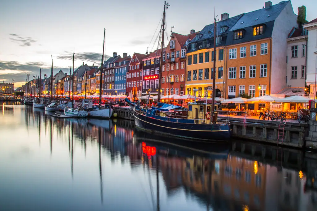 Twilight view of colorful buildings and boats at Nyhavn canal, a popular tourist attraction in Copenhagen, Denmark.