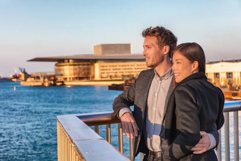 Interracial couple enjoying a sunset at Copenhagen harbourfront with a view of the Opera House, Denmark, symbolizing European travel and cultural diversity.