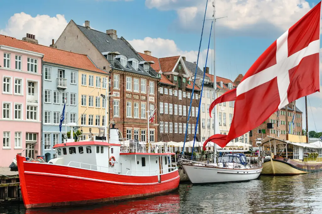 Colorful boats docked in the historic harbor of Copenhagen, Denmark with traditional buildings and a Danish flag fluttering in the breeze