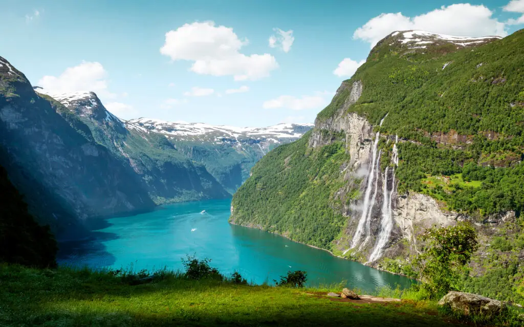 Breathtaking view of the Seven Sisters Waterfall in Geirangerfjord, Norway, showcasing lush greenery and a vibrant blue fjord.