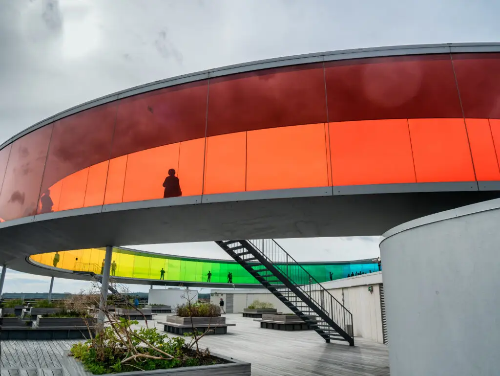 Visitors explore the colorful, circular rooftop walkway of the Aros Art Museum in Aarhus, Denmark, showcasing modern architecture and urban design.