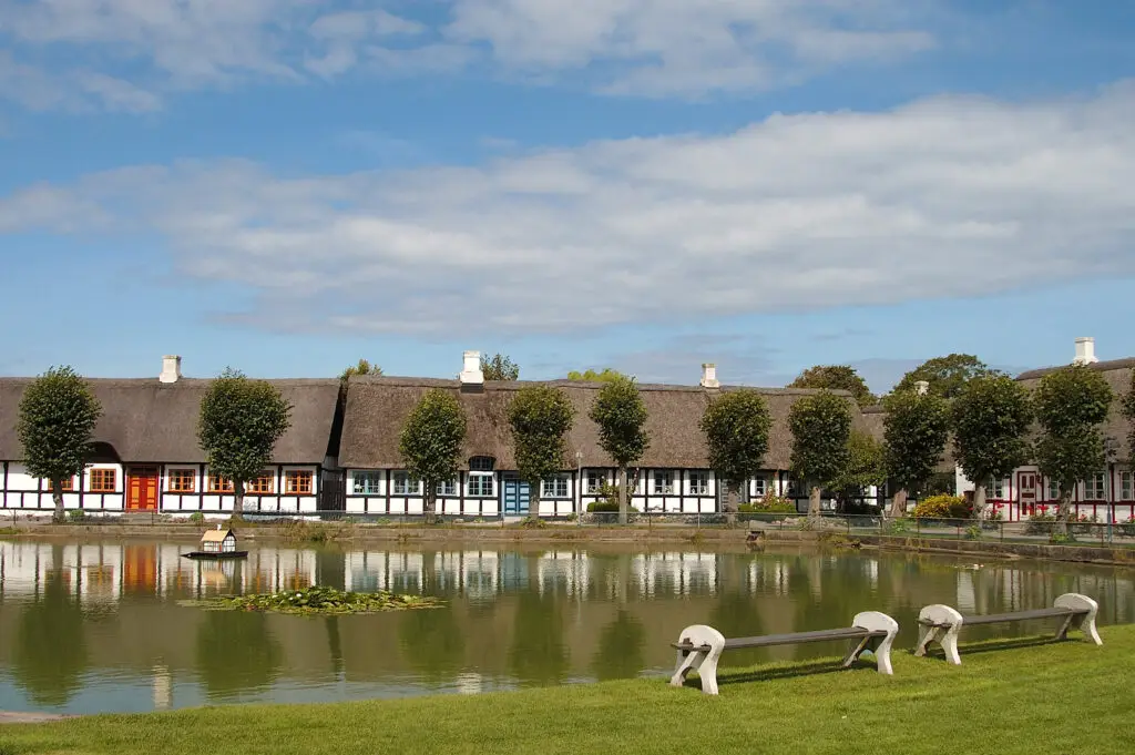 Traditional thatched-roof houses in Samsø, Denmark reflecting on a tranquil pond with lush greenery around, ideal for scenic tour spots in Scandinavia.