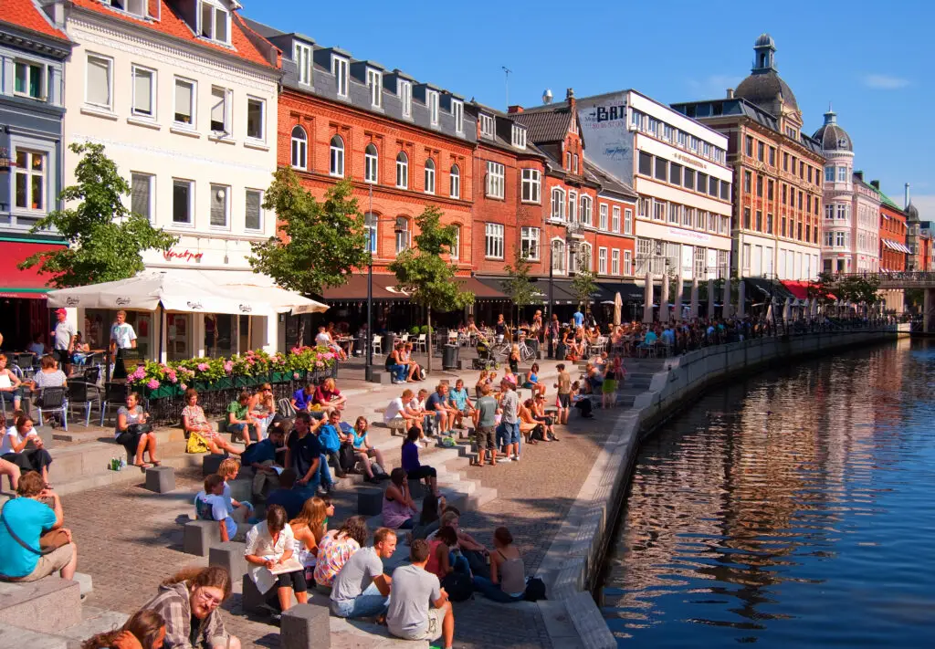 Vibrant scene at Aarhus Canal, Denmark showing lively outdoor cafes and crowds enjoying a sunny day