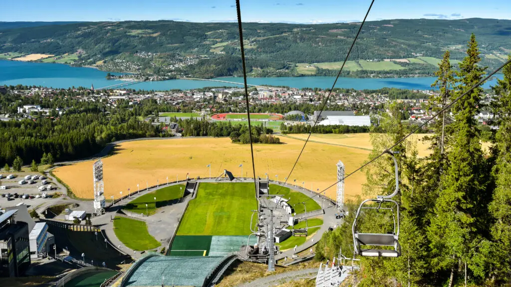 Panoramic view of Lillehammer, Norway from a ski lift showcasing the town, lake, and surrounding mountains during summer.