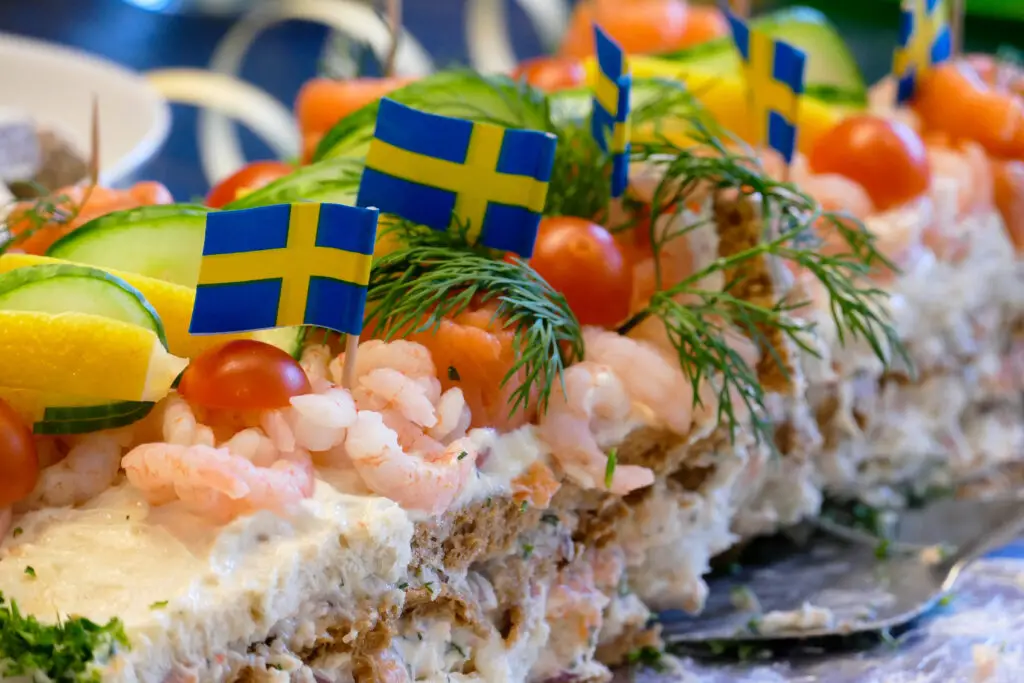 Close-up of a traditional Swedish smörgåstårta with shrimp and salmon, garnished with cucumber, lemon, tomatoes, and Swedish flags, served during a tour in Stockholm, Sweden.