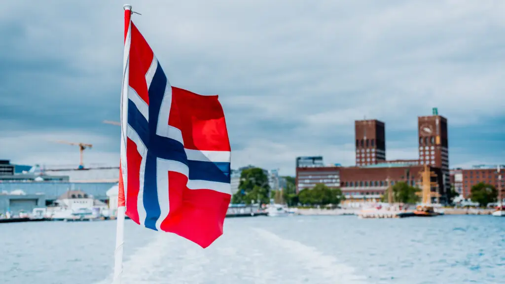 Norwegian flag waving on a ferry with a panoramic view of Oslo cityscape from the water