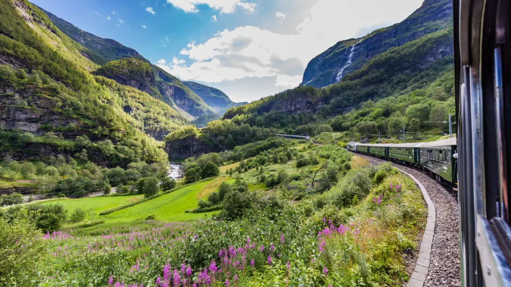 Scenic view from the Flamsbana train showcasing lush green landscapes and a waterfall in the mountains of Norway