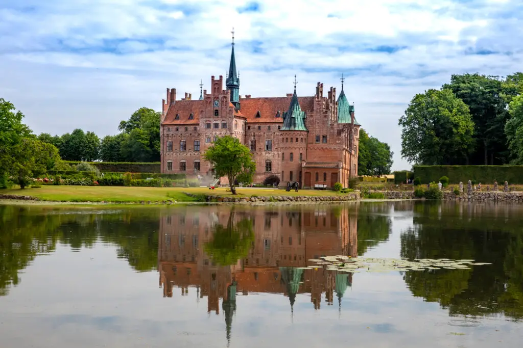 Majestic view of Egeskov Castle in Denmark reflected perfectly in a tranquil lake on a cloudy day, ideal for historical tours in Scandinavia.