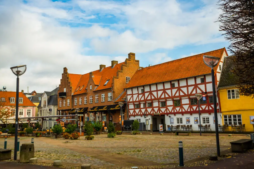 Historic street view in Aalborg, Denmark featuring traditional Danish architecture with colorful houses and a cobblestone square under a cloudy sky
