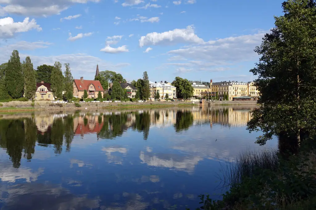 Scenic view of Klarälven river in Karlstad, Sweden showcasing calm waters reflecting colorful historical buildings and lush greenery under a blue sky with soft clouds