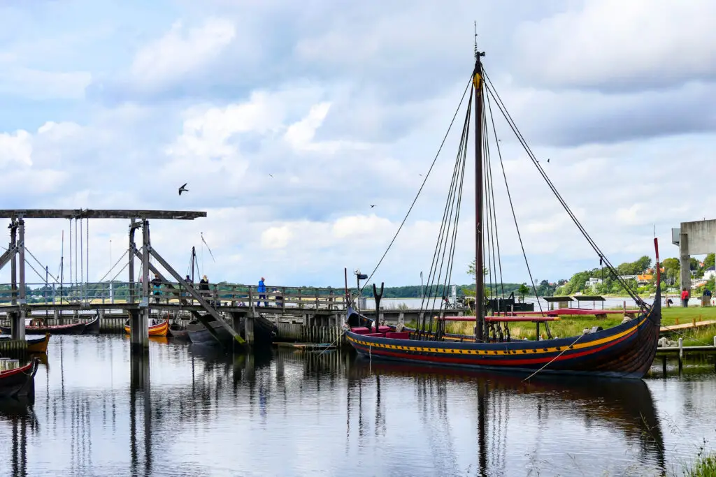 Colorful Viking ship on display at the Viking Ship Museum in Roskilde, Denmark, with a scenic view of a harbor and walking pier.