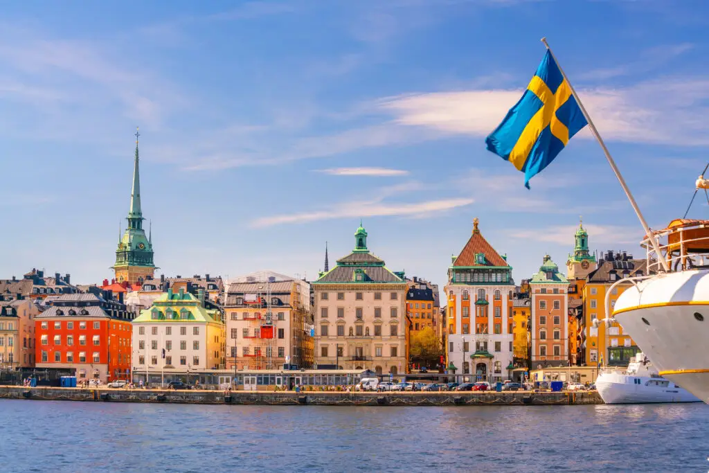 Scenic view of Stockholm's old town with vibrant buildings and the Swedish flag waving from a boat, highlighting the cityscape of Sweden.
