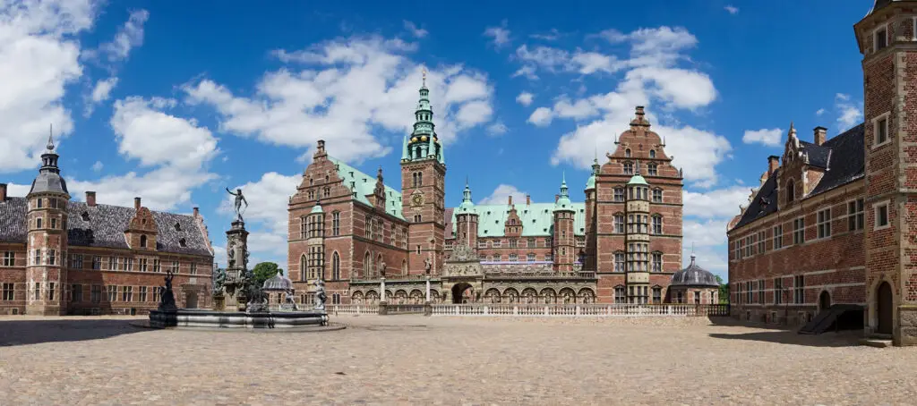 Panoramic view of Frederiksborg Castle in Hillerod, Denmark, showcasing its Renaissance architecture and Neptune Fountain on a sunny day.
