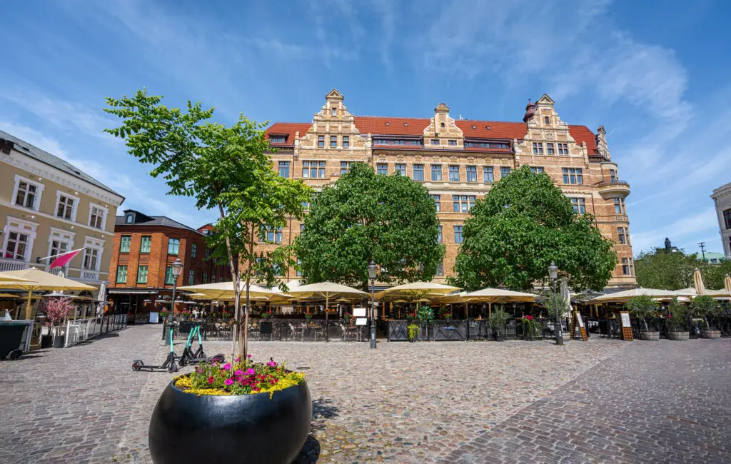 Lively scene at Lilla Torg Square in Malmo, Sweden, featuring outdoor cafes under large umbrellas, traditional cobblestone streets, and historic European architecture.