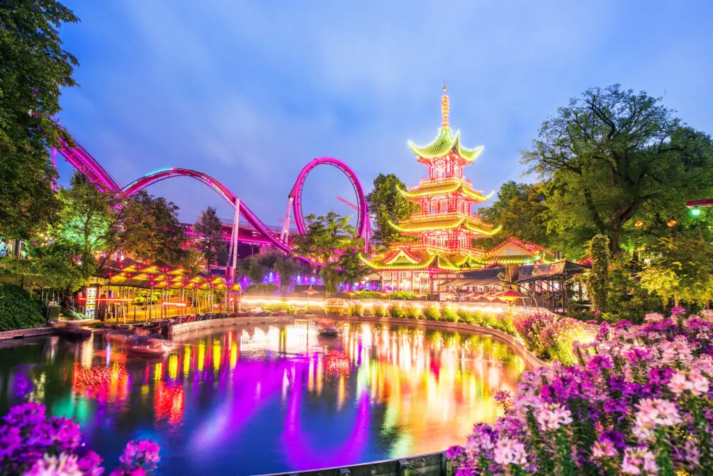Evening view of illuminated Tivoli Gardens with vibrant lights and reflections in Copenhagen, Denmark, showcasing popular tourist attractions and exotic landscapes.
