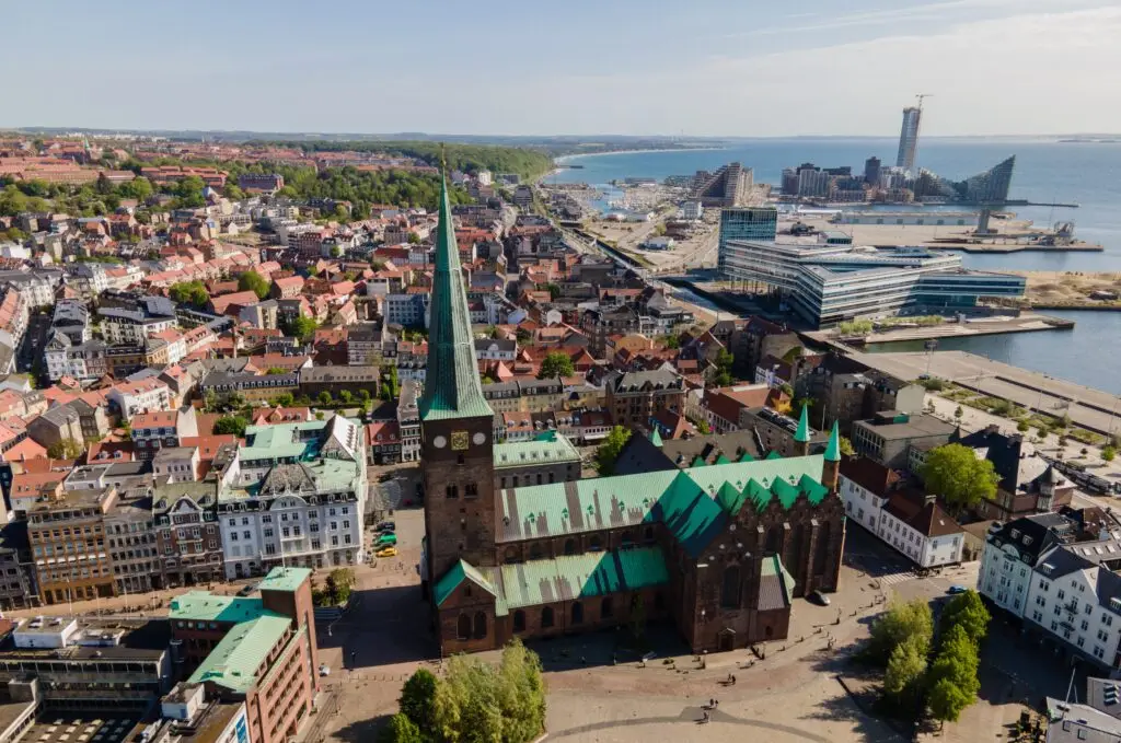 Aerial view of Aarhus Cathedral (Domkirke) in Aarhus, Denmark, surrounded by historic cityscape and modern architecture near the coastline.