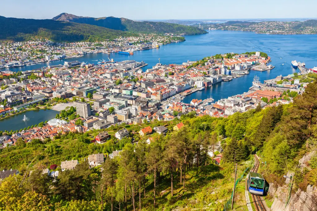 Panoramic view of Bergen city with funicular railway ascending Mount Fløyen, showcasing the vibrant architecture and the surrounding Norwegian fjords.
