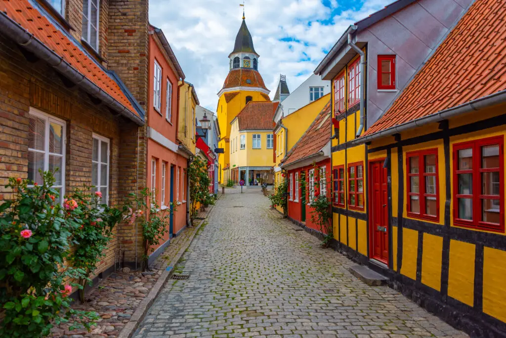 Yellow clock tower at the end of a cobblestone street flanked by colorful traditional Danish houses in Faaborg, Denmark, showcasing Scandinavian architectural charm.