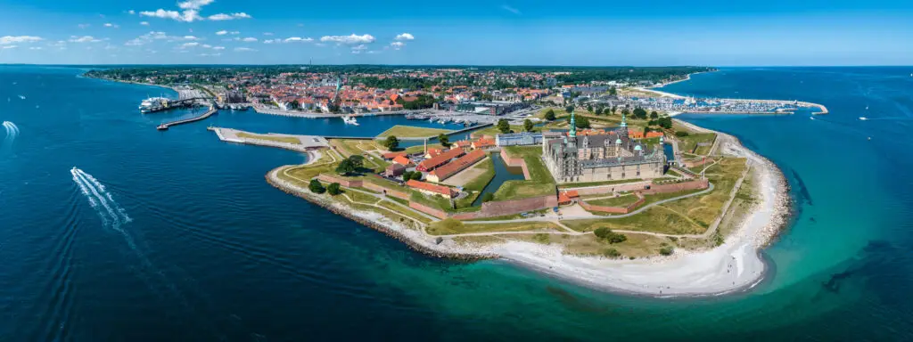 Aerial view of the historic Kronborg Castle in Denmark, showcasing its strategic ramparts and ravelin at the entrance of the Baltic Sea, with a bustling marina and town in the background.