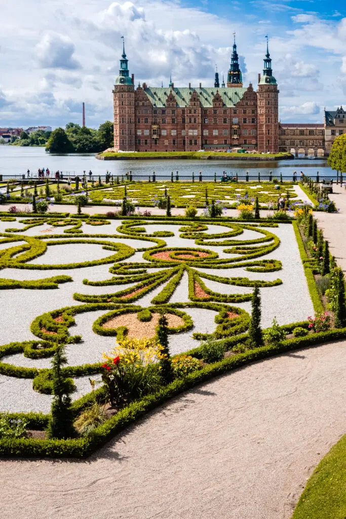 Alt Text: Ornate gardens with geometric hedge designs and bright flowers at Frederiksborg Castle in Copenhagen, perfect for a scenic tour in Scandinavia.