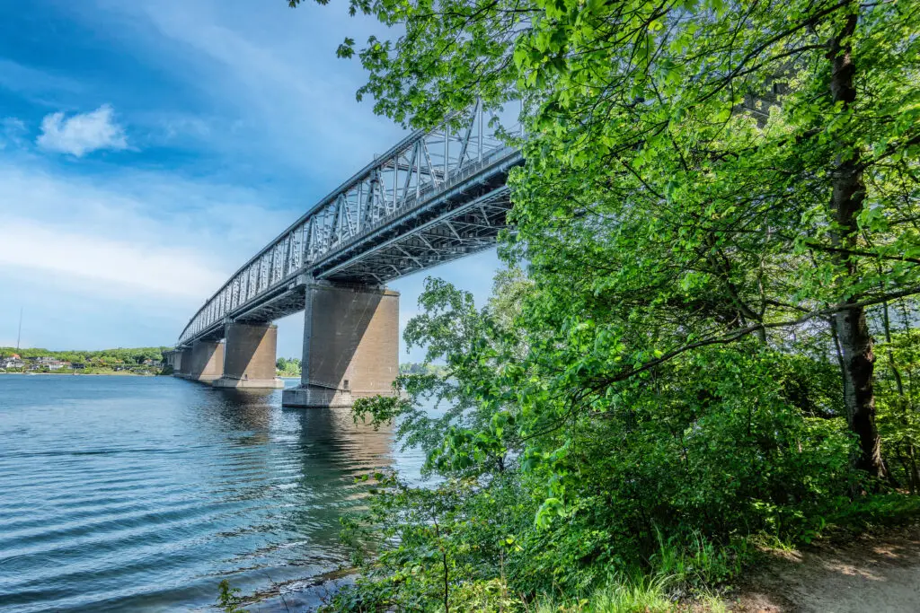 Old bridge over Little Belt viewed from a lush green forest in Middelfart, Denmark, showcasing the architectural marvel and natural beauty ideal for tourism.