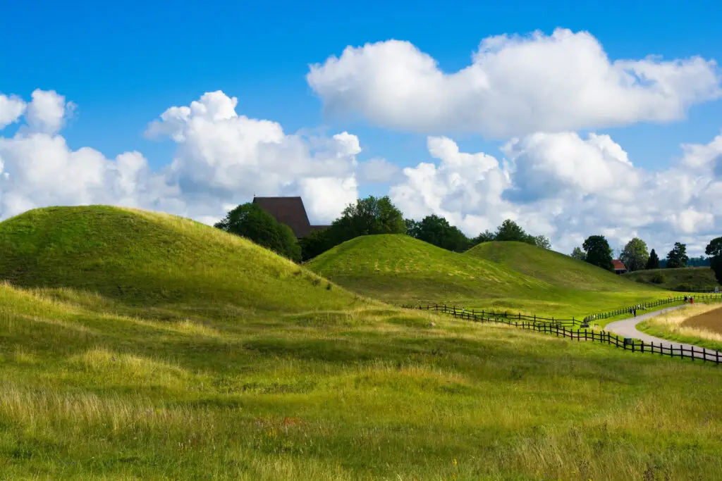 Scenic view of the historic Royal Mounds at Gamla Uppsala, Sweden, under a bright blue sky, illustrating a famous tourist spot in Scandinavia.