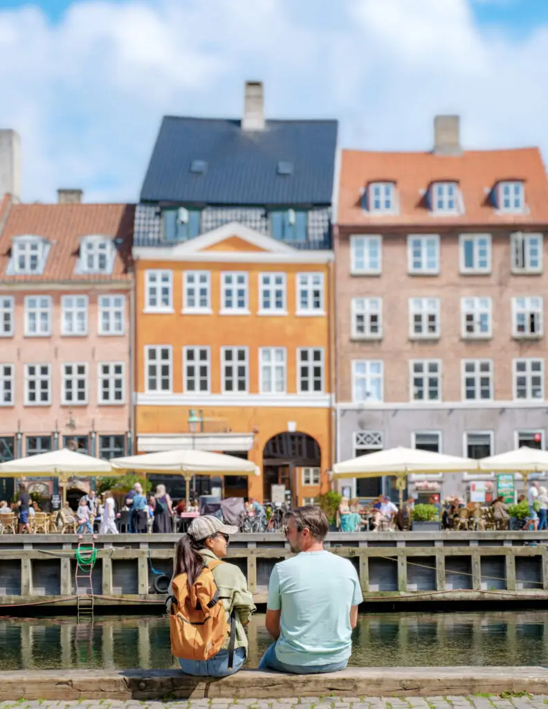Copenhagen Couple chatting by the canal, colorful historic buildings in the background