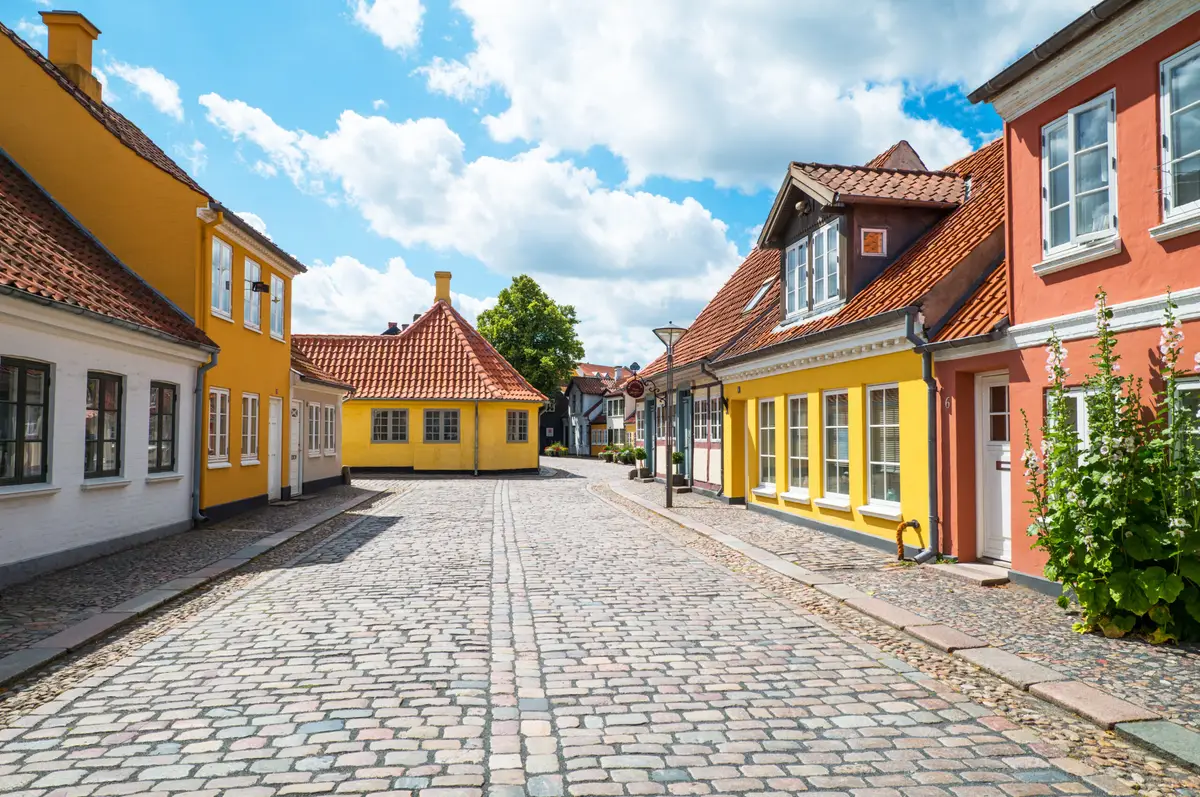 Charming view of a cobblestone street lined with traditional colorful houses under a clear blue sky in Denmark, perfect for cultural tourism.