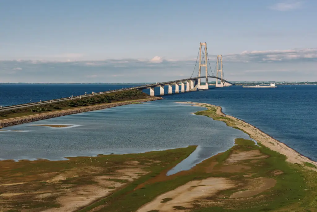 Scenic view of the Great Belt Bridge in Denmark, spanning the blue waters with a lush green coastline under a clear sky.