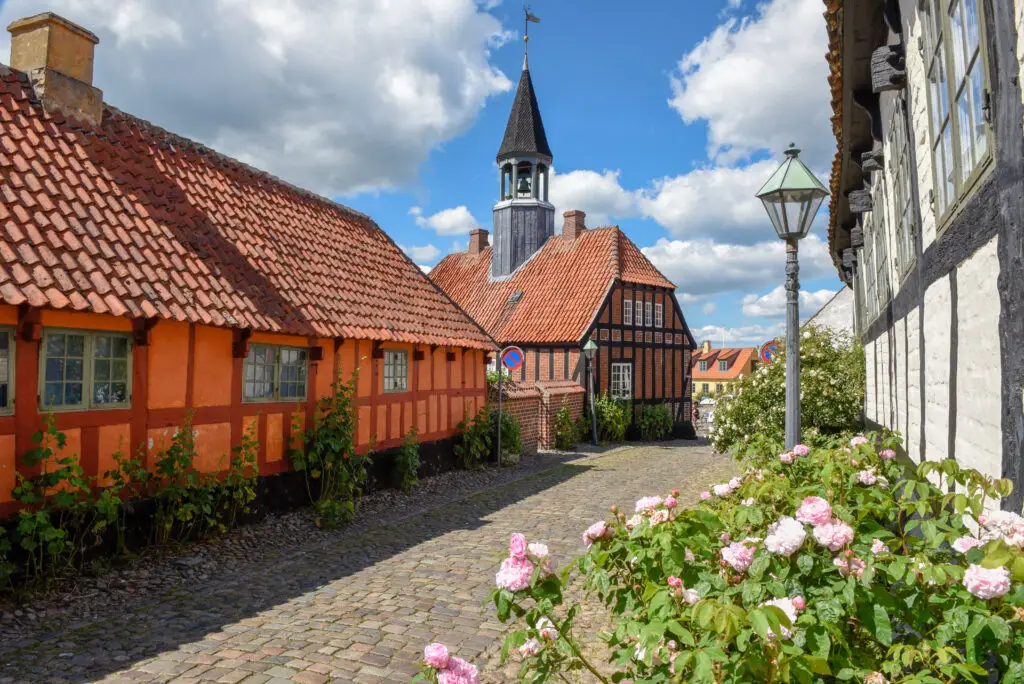 Traditional historic village of Ebeltoft in Denmark showcasing charming cobblestone streets, vibrant orange-roofed buildings, and the iconic town church.