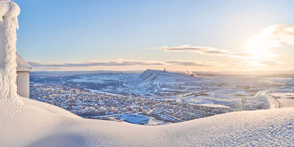 Panoramic winter view of Kiruna city with the prominent iron ore mine on Kiirunavaara mountain, as observed from Luossavaara peak, under a glowing sunset, Northern Sweden.