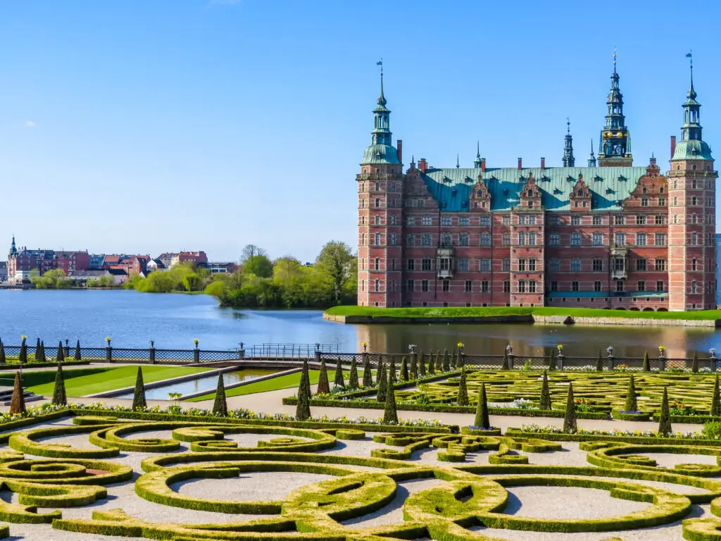 View of Frederiksborg Slot palace and gardens in Hillerod, Denmark, showcasing the ornate architecture and landscaped formal gardens on a sunny day.